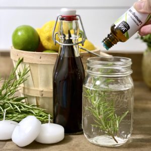 Adding essential oil drops to the water and rosemary inside the mason jar.