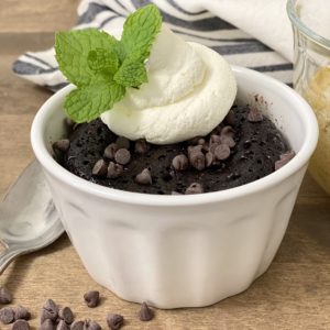 A delicious chocolate mug cake with a dollop of whipped cream and a mint sprig.