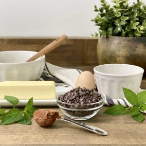The ingredients needed to make a chocolate mug cake including chocolate, butter, egg, sugar, a ramekin, and more.