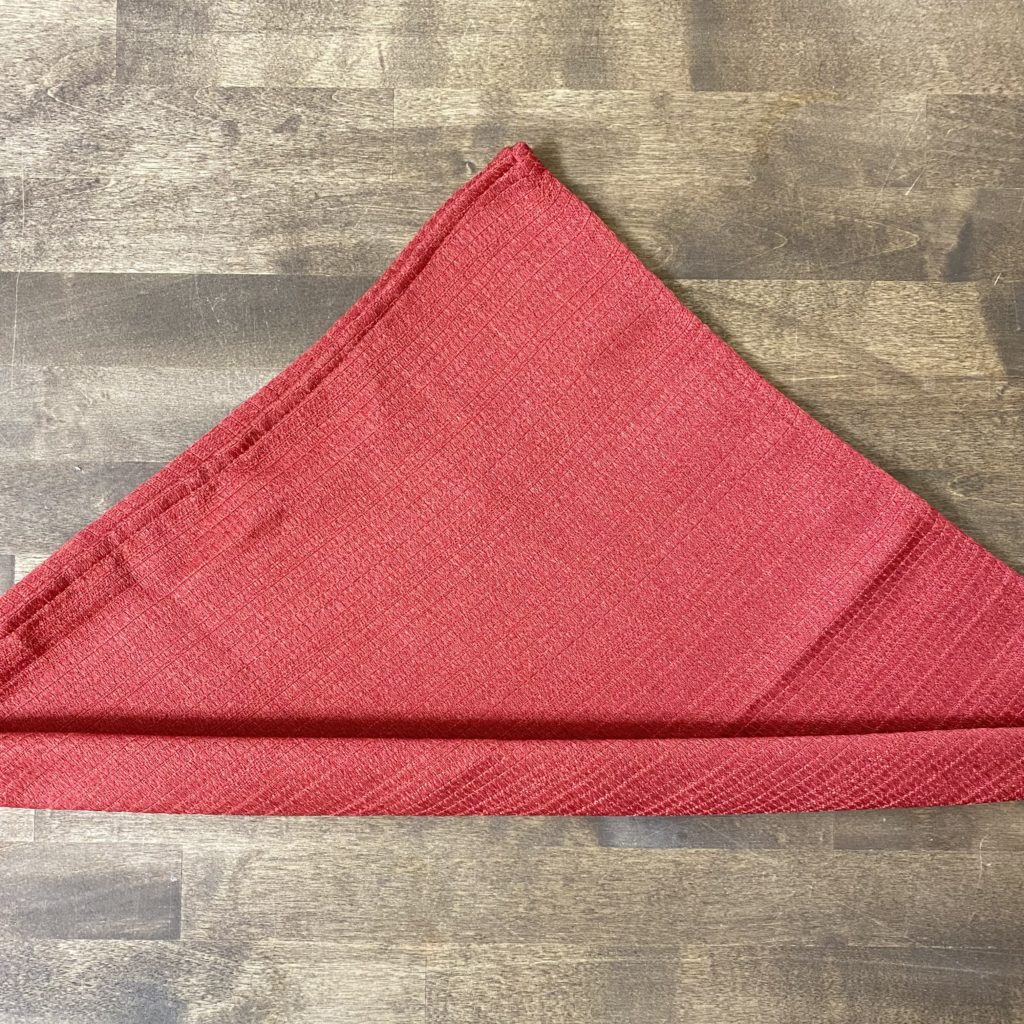 Rolling up a red cloth napkin from the bottom of the triangle.
