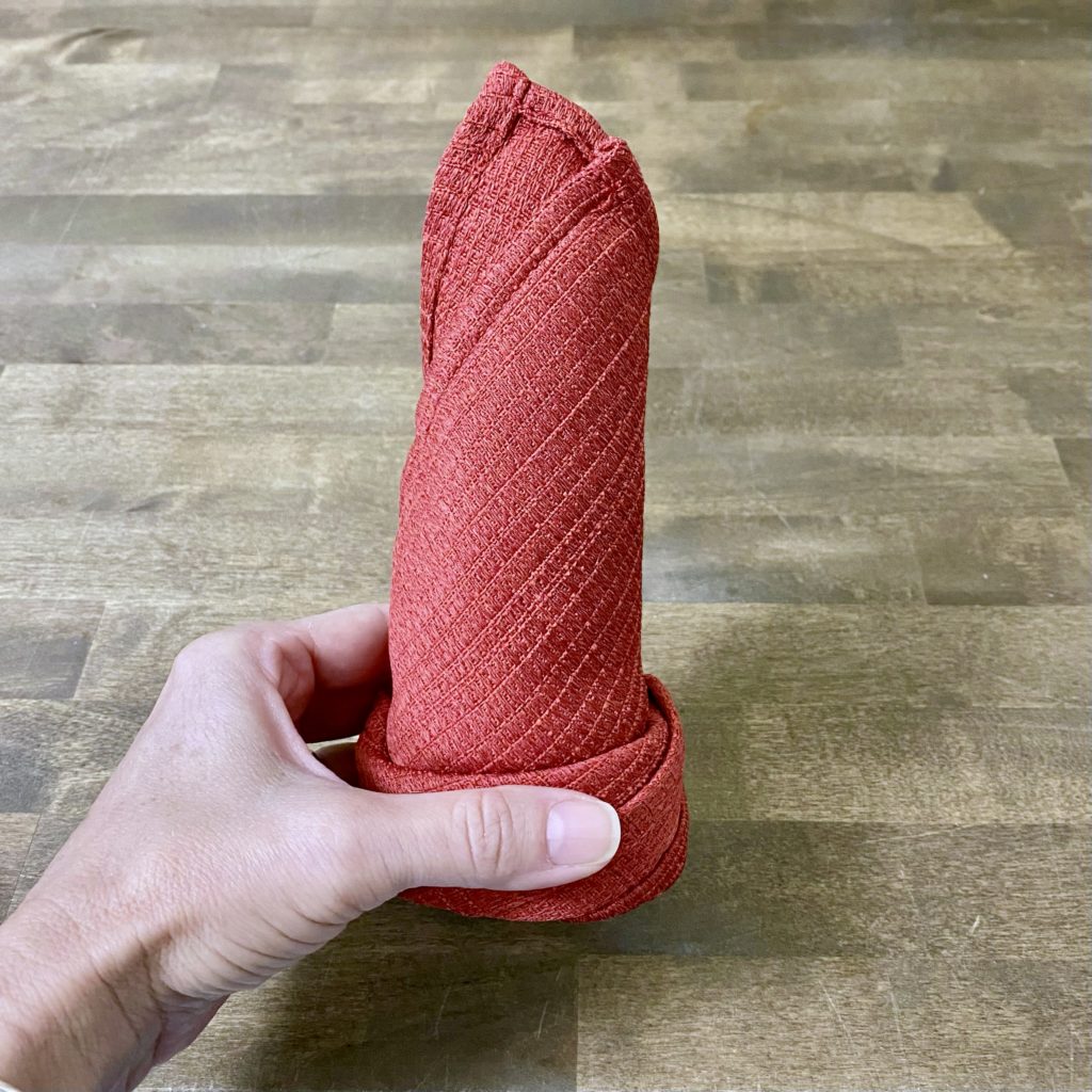 Holding the red cloth napkin up after it’s been rolled and secured.