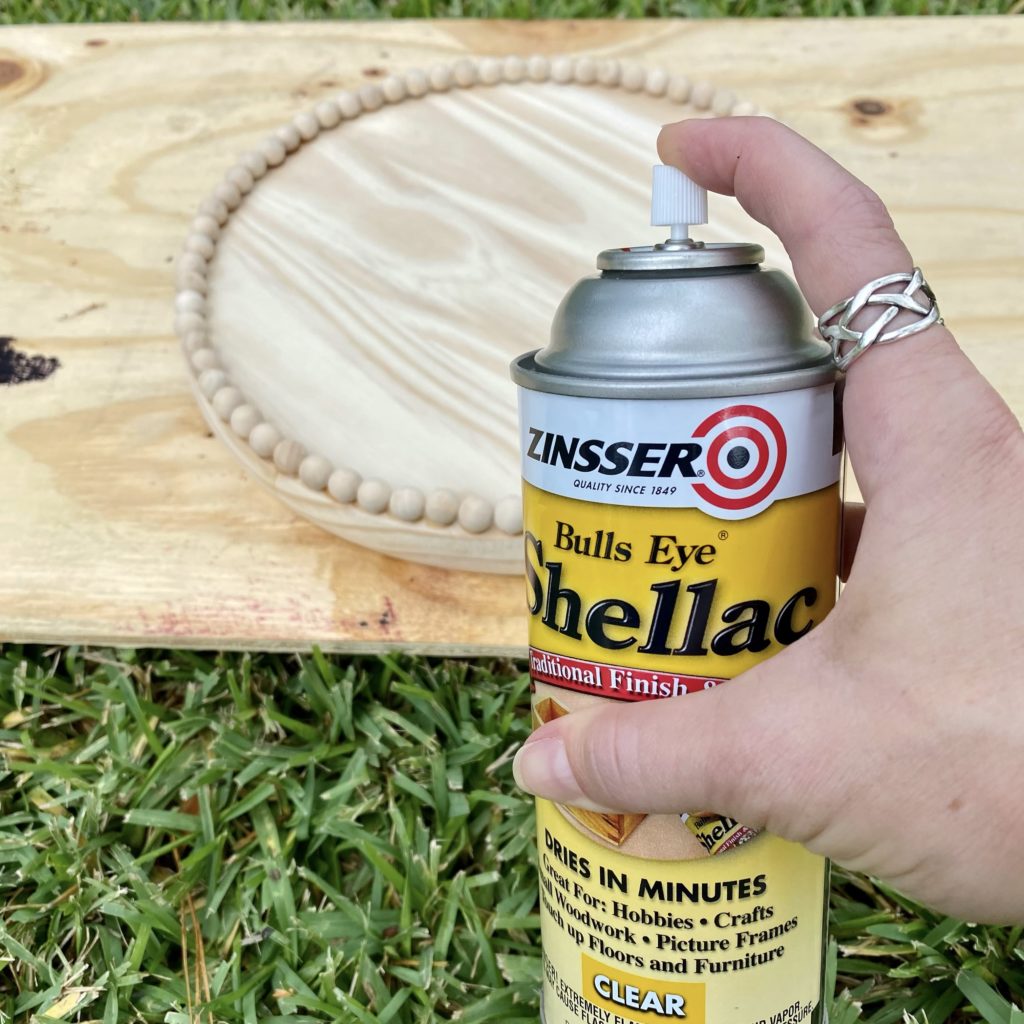Spraying Shellac sealer onto the wood piece outside.