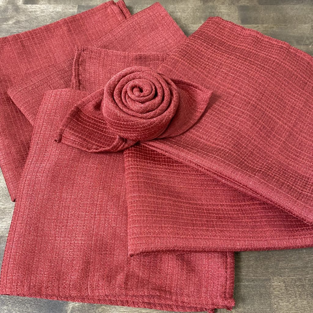 Red cloth napkins laid out on a table with one folded into a rose on top.