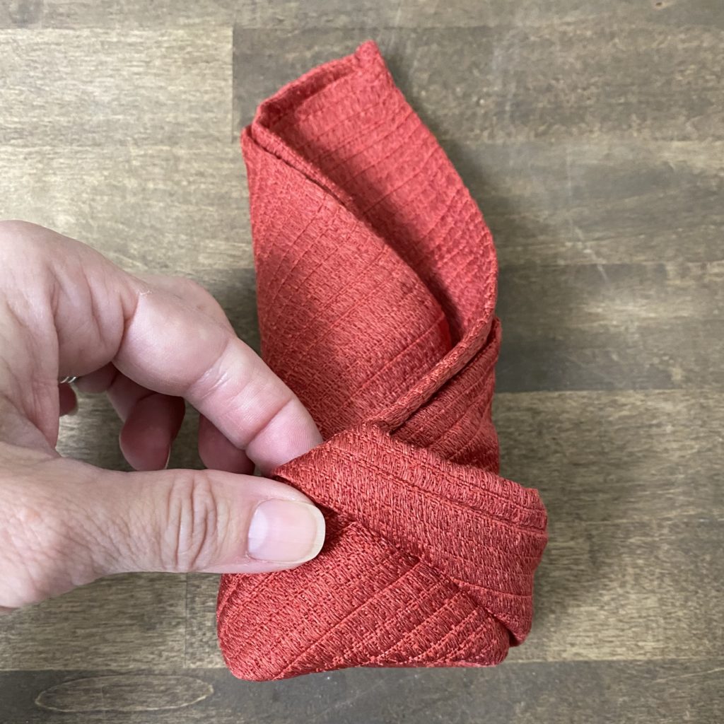 Tucking the end of the rolled napkin into the pocket to secure the roll in place. 