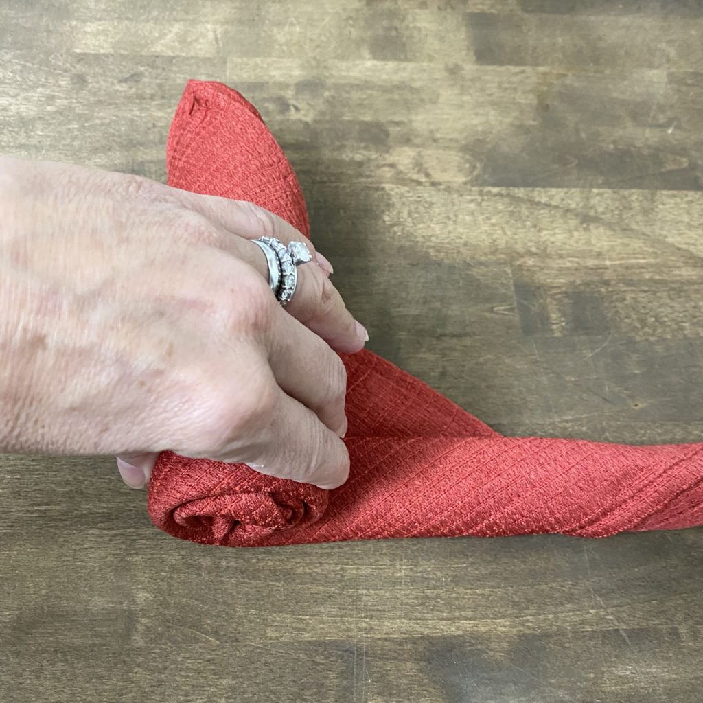 Rolling a red cloth napkin to form a rose.