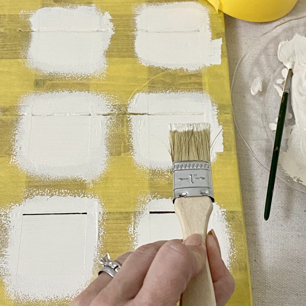 Painting the checker squares onto the game board using white paint on a paint brush.