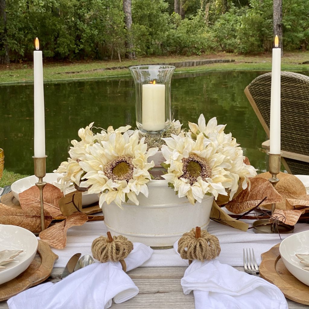 Centerpiece for a casual fall outdoor gathering with faux white sunflowers and a candle.