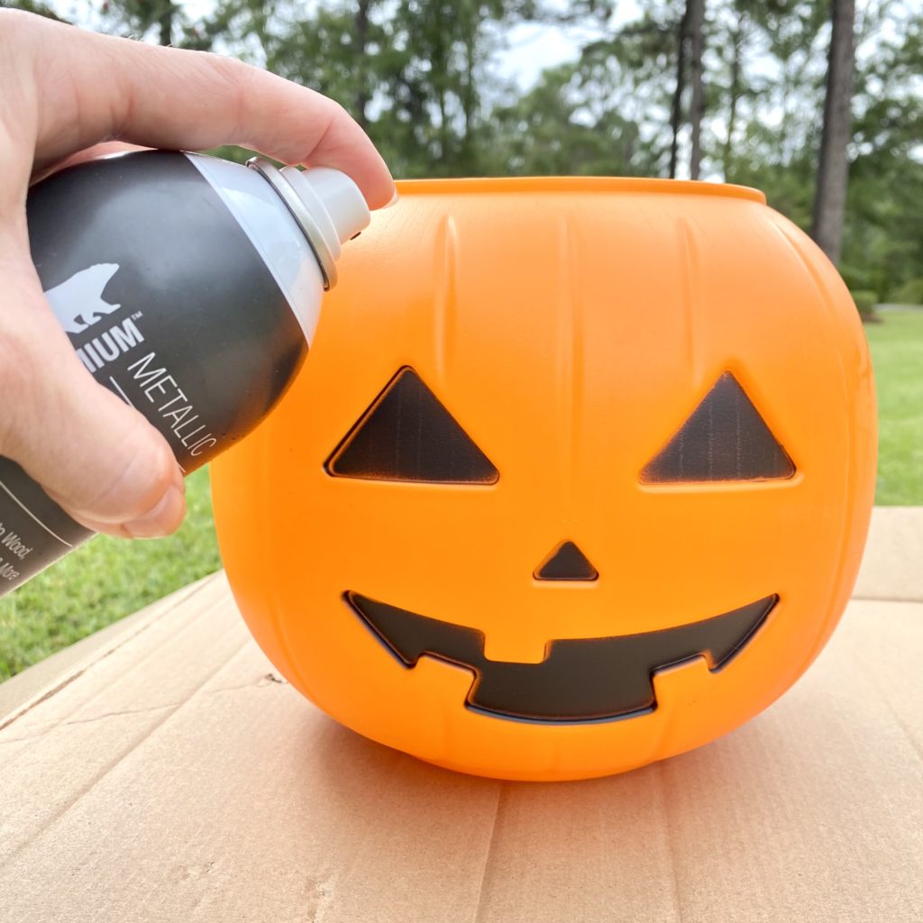 Spraying the outside of the Jack O’Lantern trick-or-treat pail with spray paint outside.