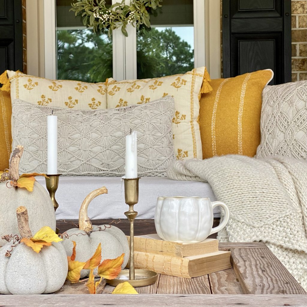 View of one side of the porch swing with early fall pillows, blanket, and concrete pumpkins on the coffee table. 