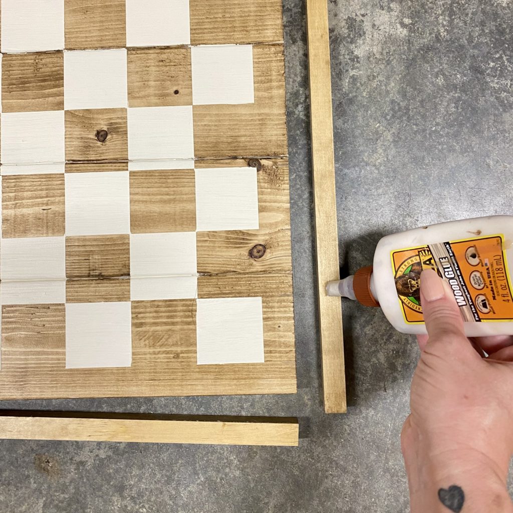 Gluing the framing pieces on the DIY Checker Board with wood glue.
