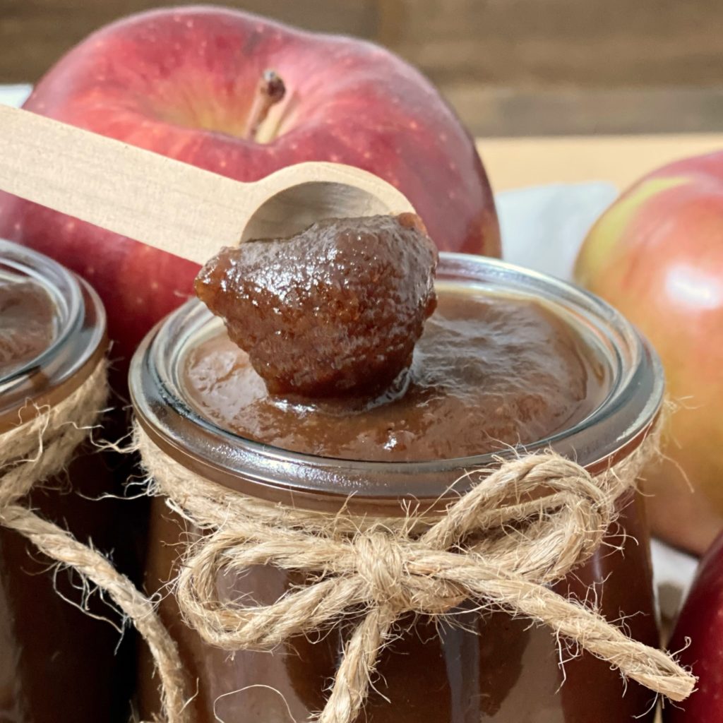 Easy crockpot apple butter on a small wood spoon with a jar of apple butter under it.