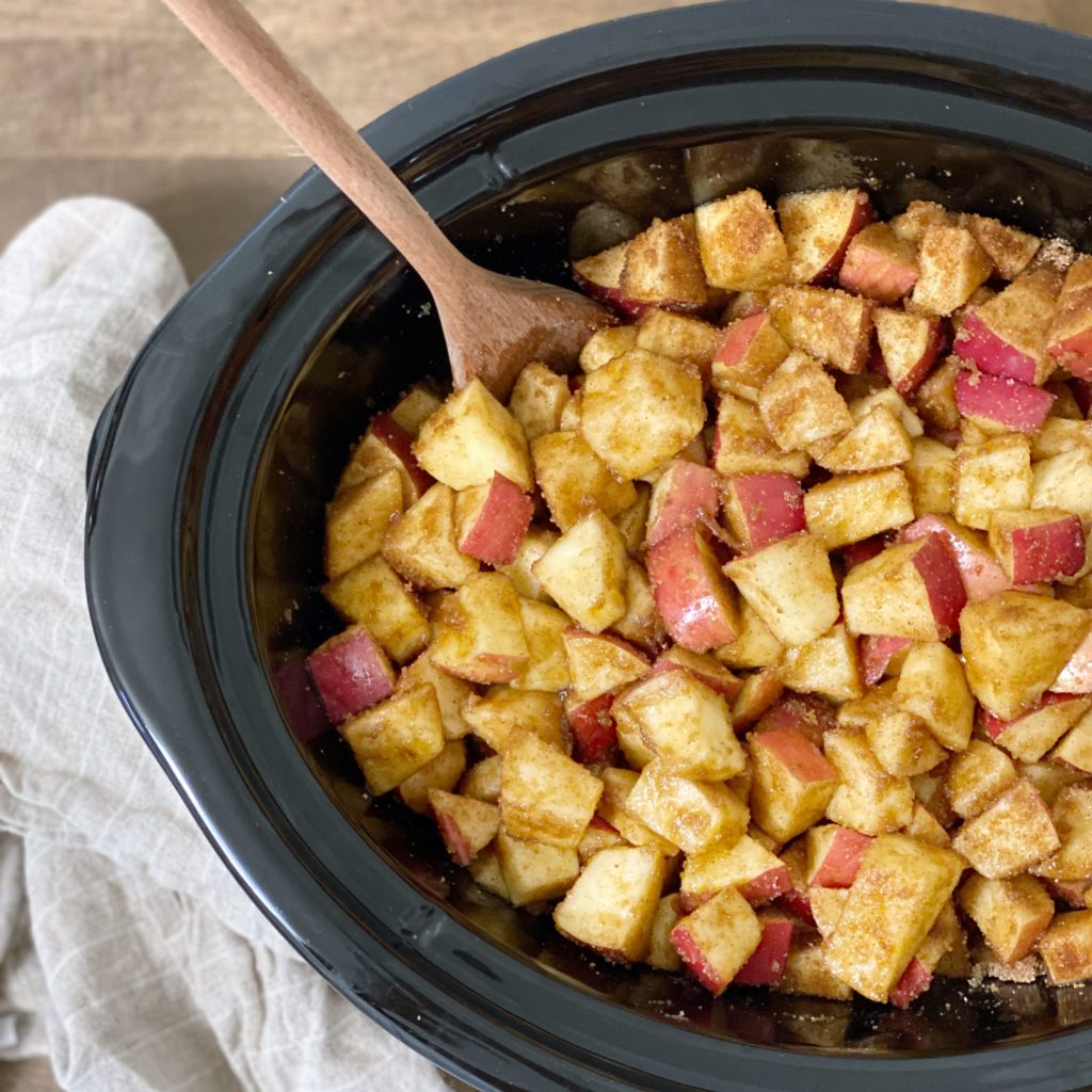 Apples and cinnamon in a crockpot with a wooden spoon.