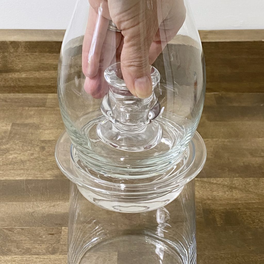 Placing the small glass taper candle holder inside the glass vase to hold the candle in the hurricane lamp.