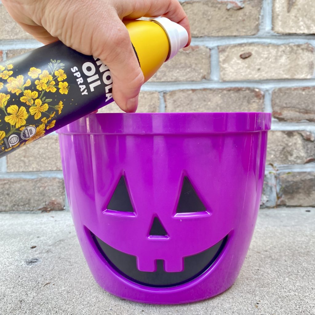 Spraying the inside of a Jack O’Lantern trick-or-treat pail with cooking spray.