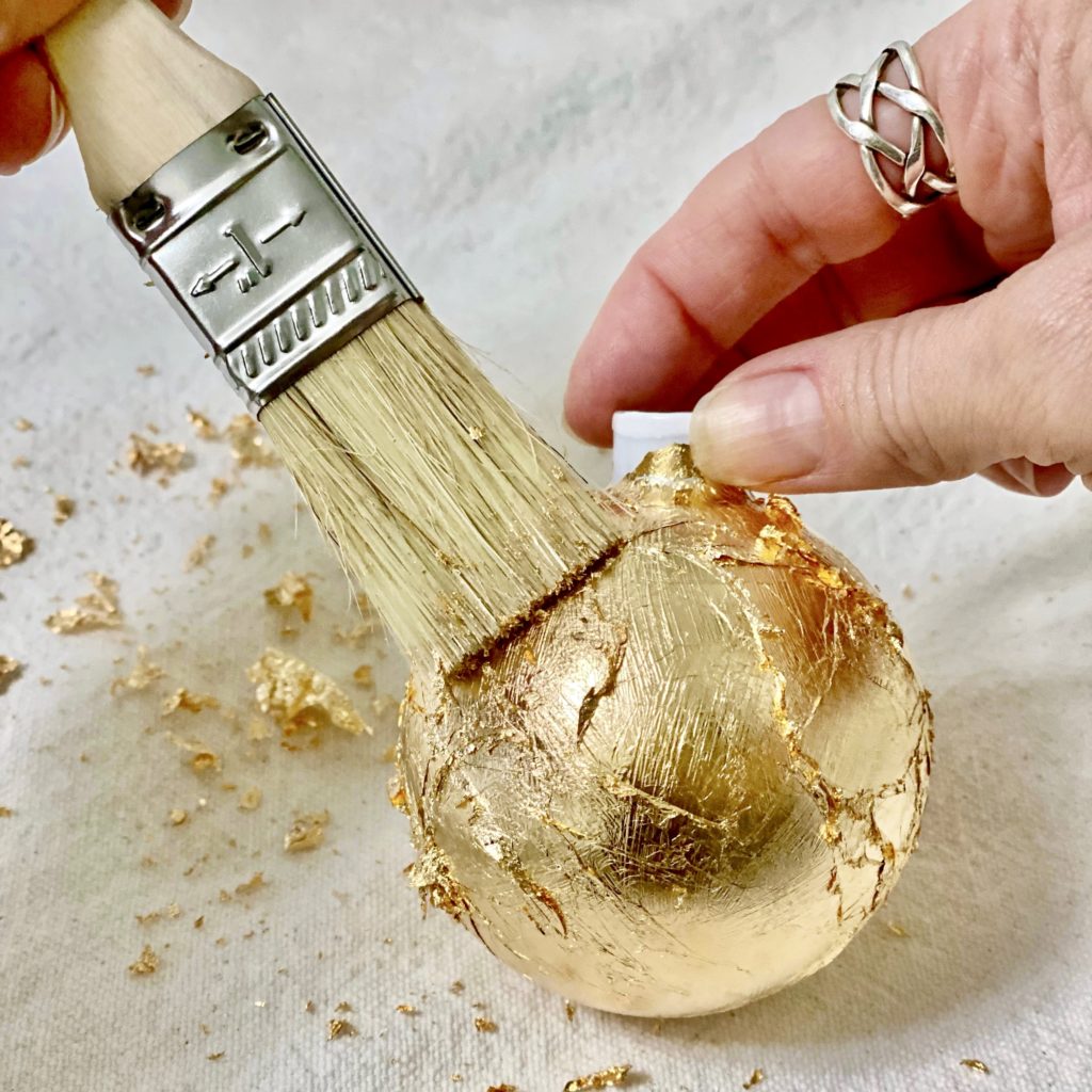 Using a dry paintbrush to brush off the gold leaf flakes from the ornament.