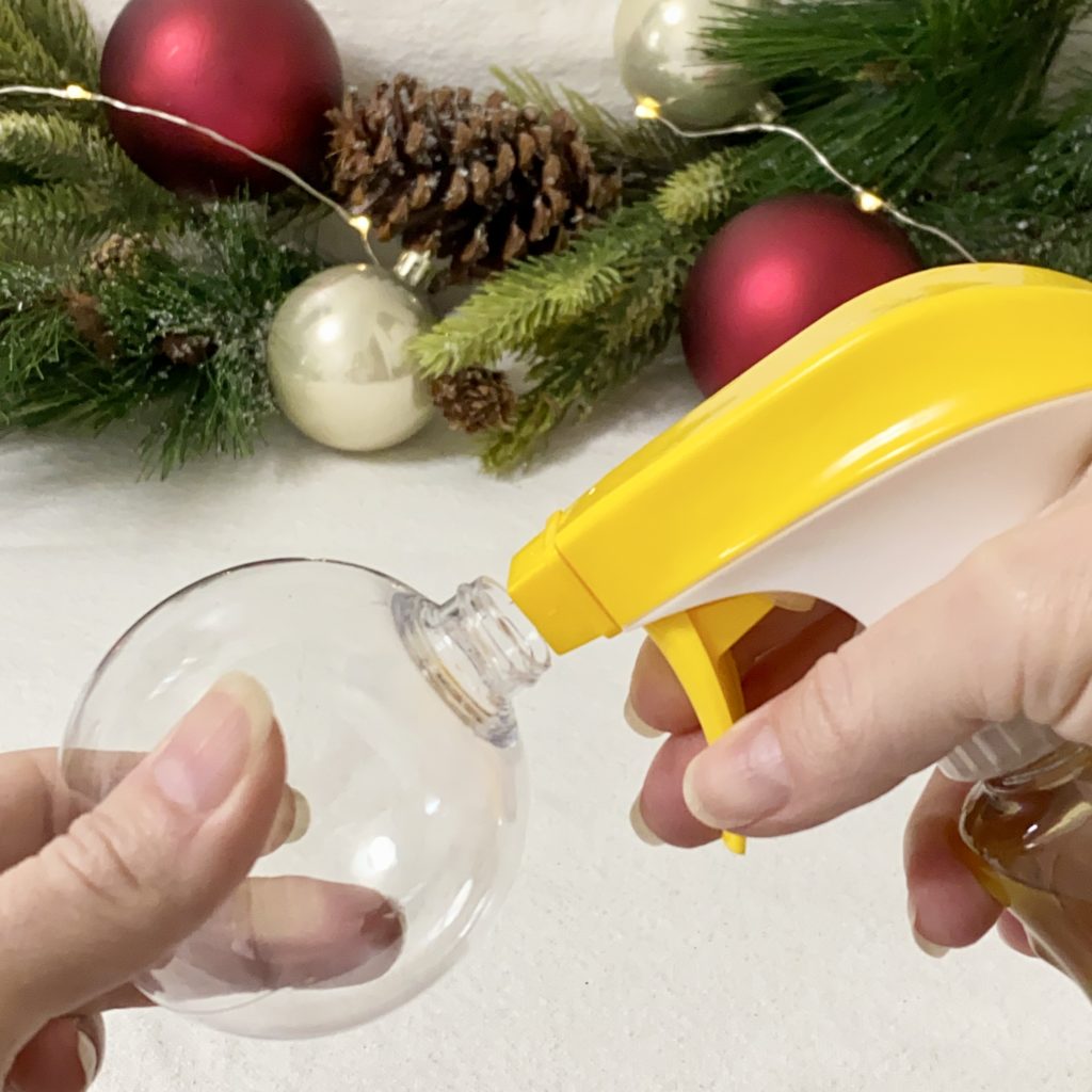 Spraying wood oil into a clear plastic ornament.