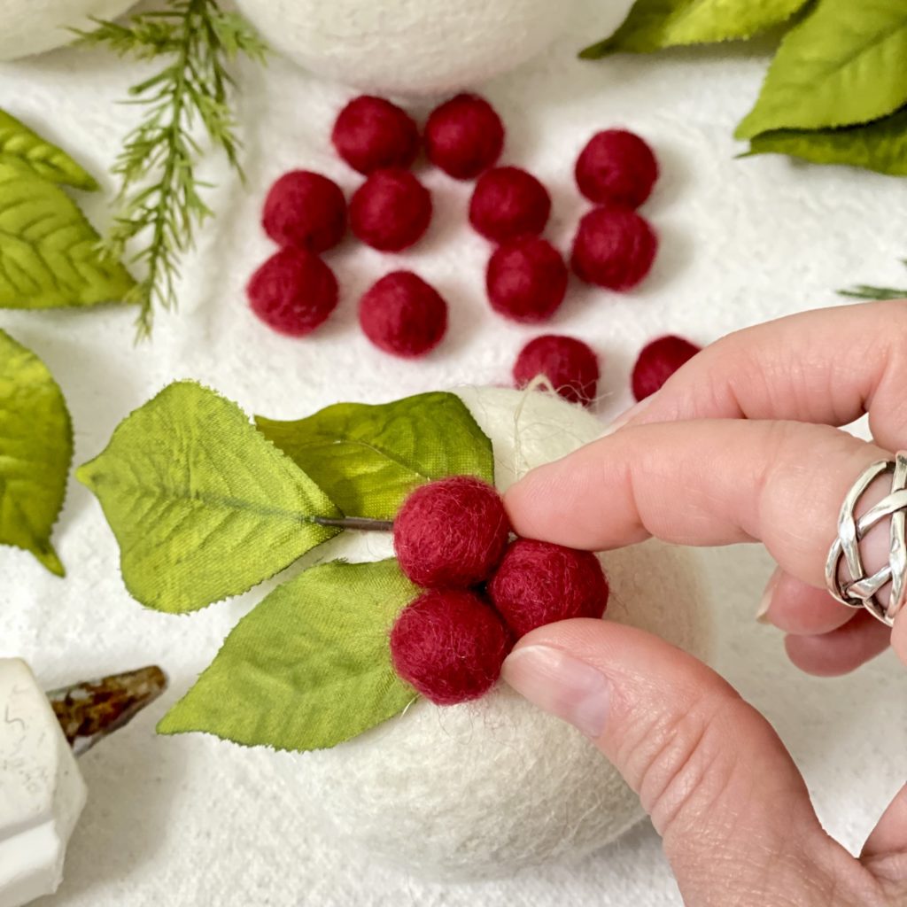 Attaching the third and final small red felt ball to the ornament to finish off the berries.