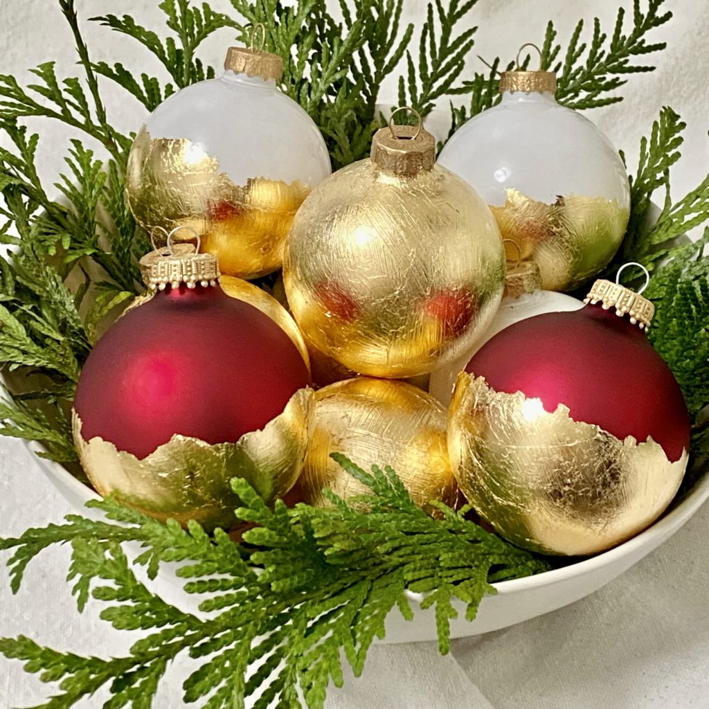DIY gold leaf Christmas tree ornaments in a bowl with greenery.