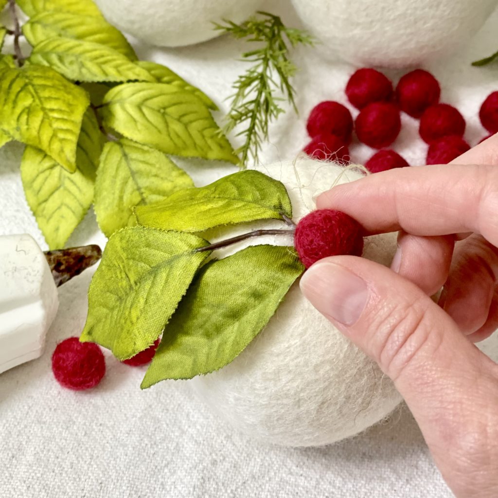 Attaching a small red felt ball onto the ornament next to the green leaves.