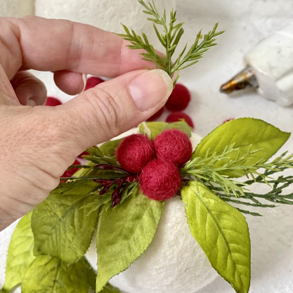Adding faux green pine to the ornament to fill in any gaps between the red berries and the leaves.