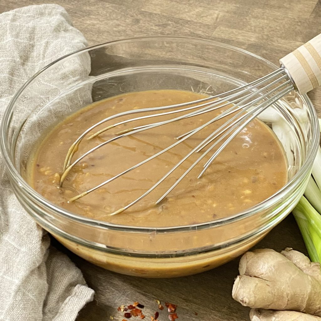The peanut sauce in a glass bowl with a whisk.