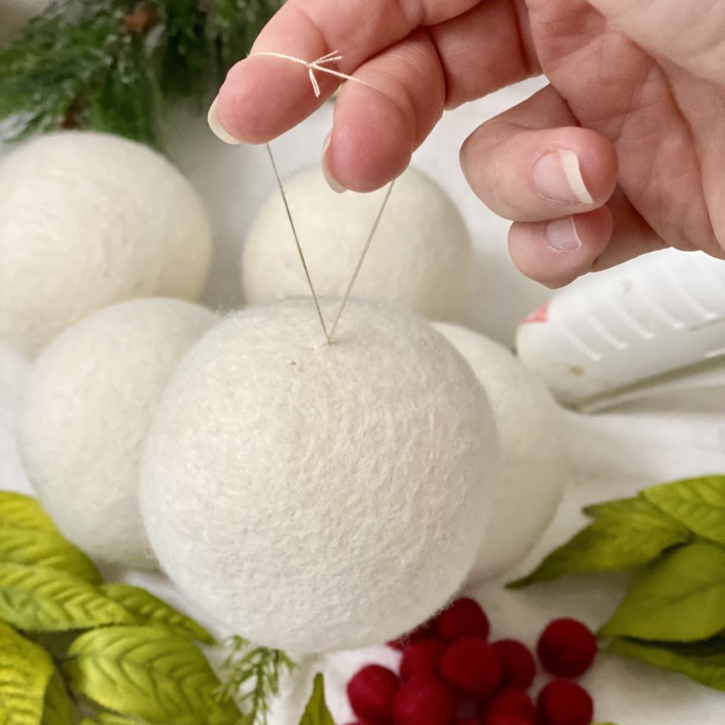 The white wool dryer ball hanging from a loop made with a needle and thread.