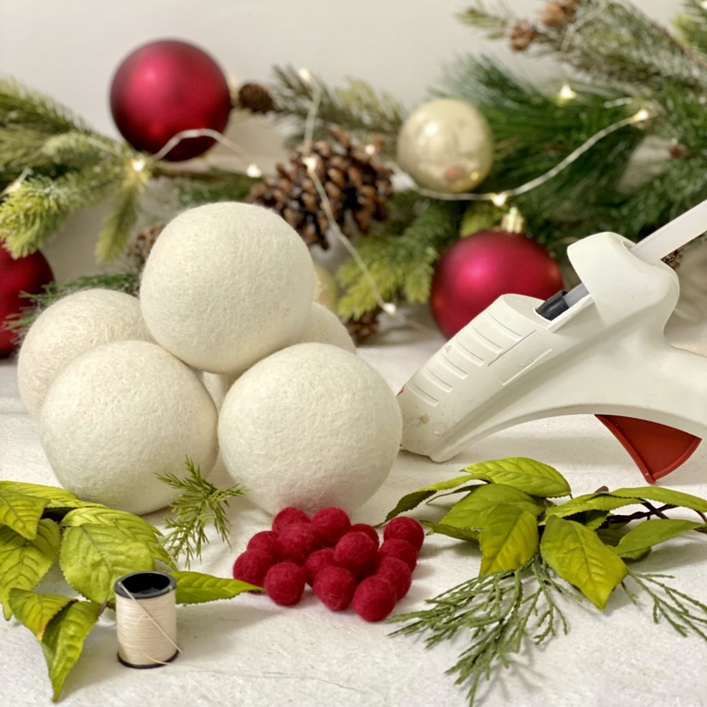 Everything needed to make felt ball Christmas tree ornaments including faux greenery, wool dryer balls, small red felt balls, and hot glue.