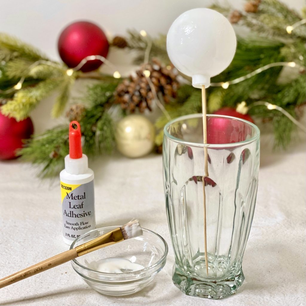 Ornament with adhesive on it drying on a skewer in a glass.