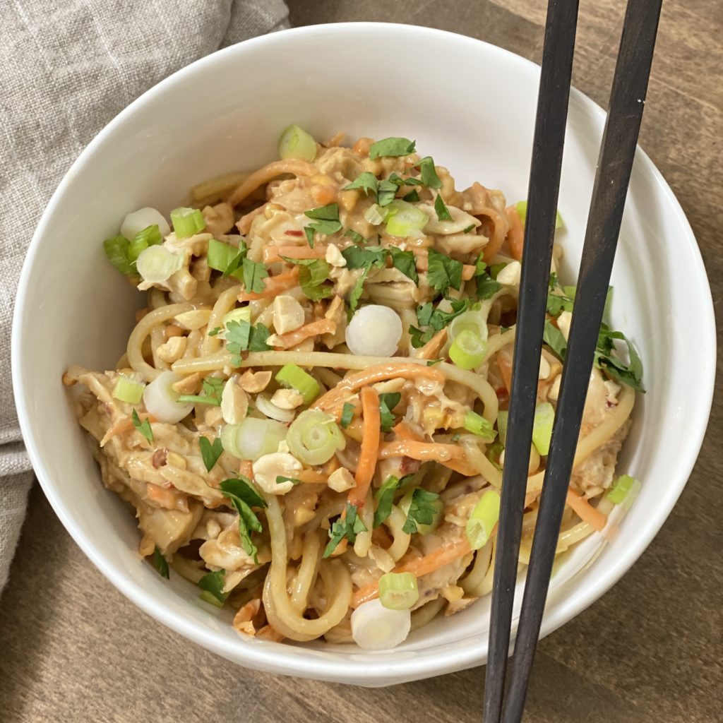 Chicken and noodles with peanut sauce in a white bowl with chopsticks.