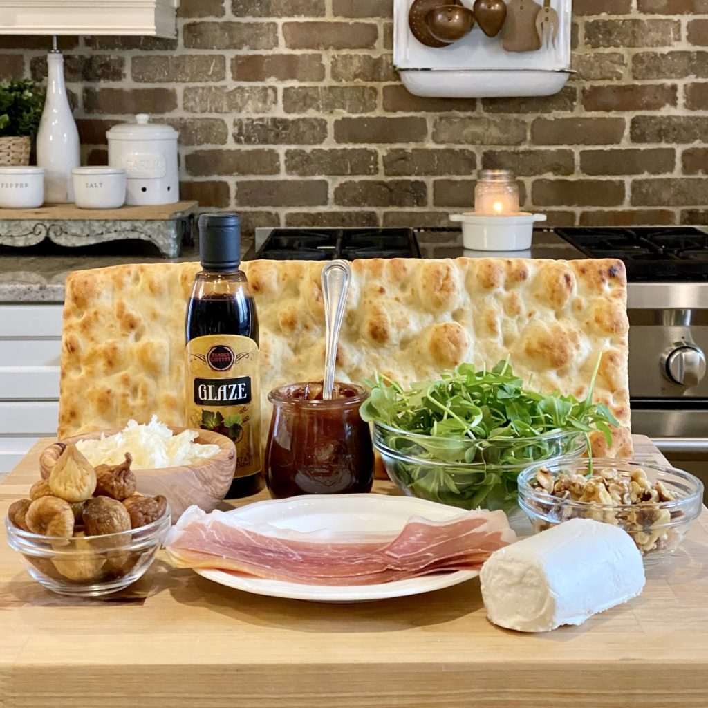 Everything you need to make Prosciutto and Fig Flatbread including Holiday Cranberry Apple Butter, flatbread, prosciutto, dried figs, goat cheese, Parmesan cheese, arugula, and walnuts.