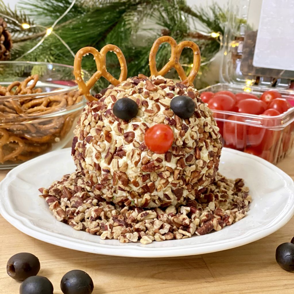 Rudolph Christmas Cheese Balll non a plate with pecans. Pretzels and grape tomatoes are in the background.