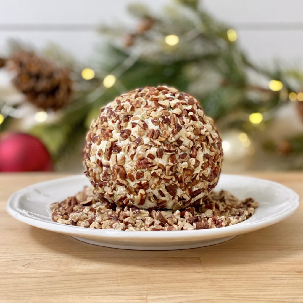 Cheese ball rolled in toasted pecans on a white plate.