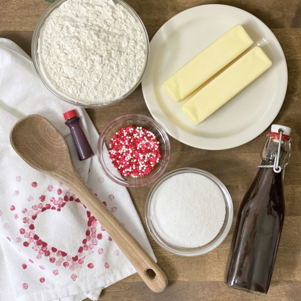 The ingredients needed to make sweet Valentine shortbread bites including flour, sugar, butter, vanilla, and sprinkles.
