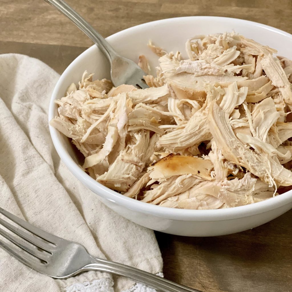 Shredded rotisserie chicken in a white bowl with forks.