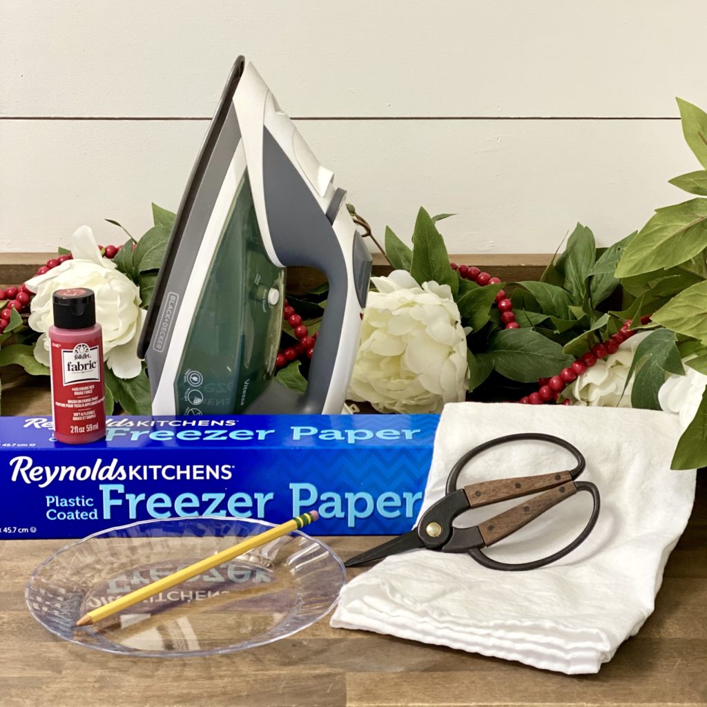 Everything you need to make easy and beautiful Valentine dish towels including a flour sack towel, fabric paint, freezer paper, a pencil, scissors, and an iron.