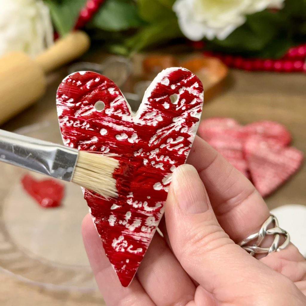 Painting a clay heart Valentine’s decoration with crimson red acrylic paint.
