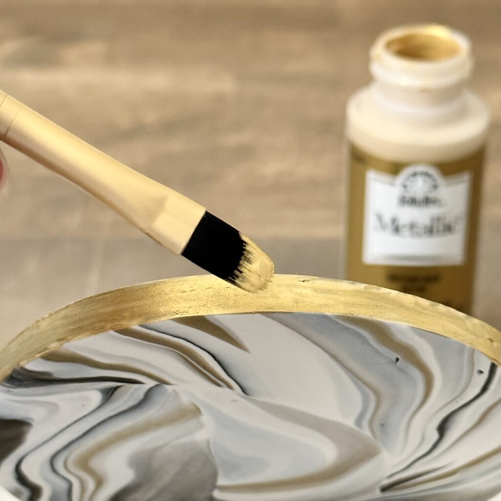 Painting the edge of a marbleized polymer clay coaster with gold acrylic paint.