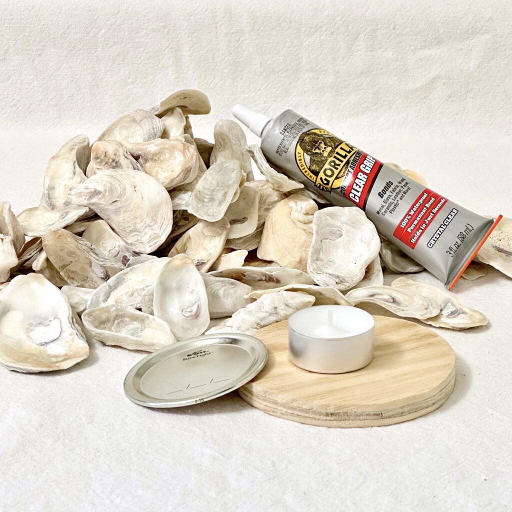 Materials needed to make an oyster shell candle holder including oyster shells, Gorilla glue, a circular piece of wood (for base), mason jar lid, and a votive candle.