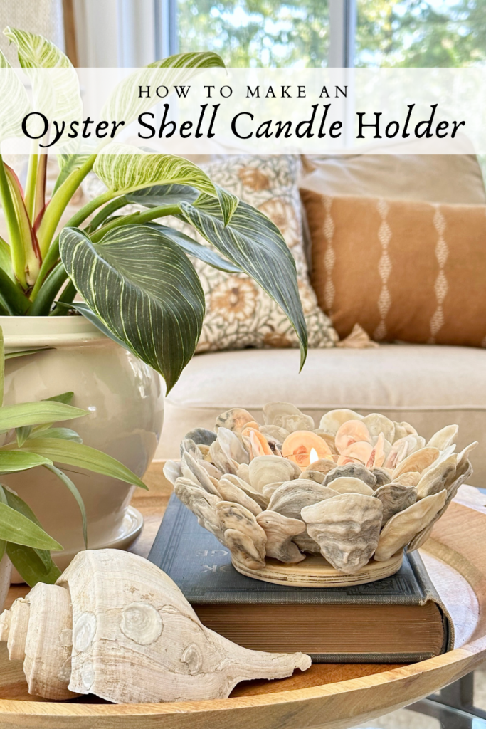 Pinterest Pin for How to Make an Oyster Shell Candle Holder with a photo of the piece styled on a tray with plants and a book.