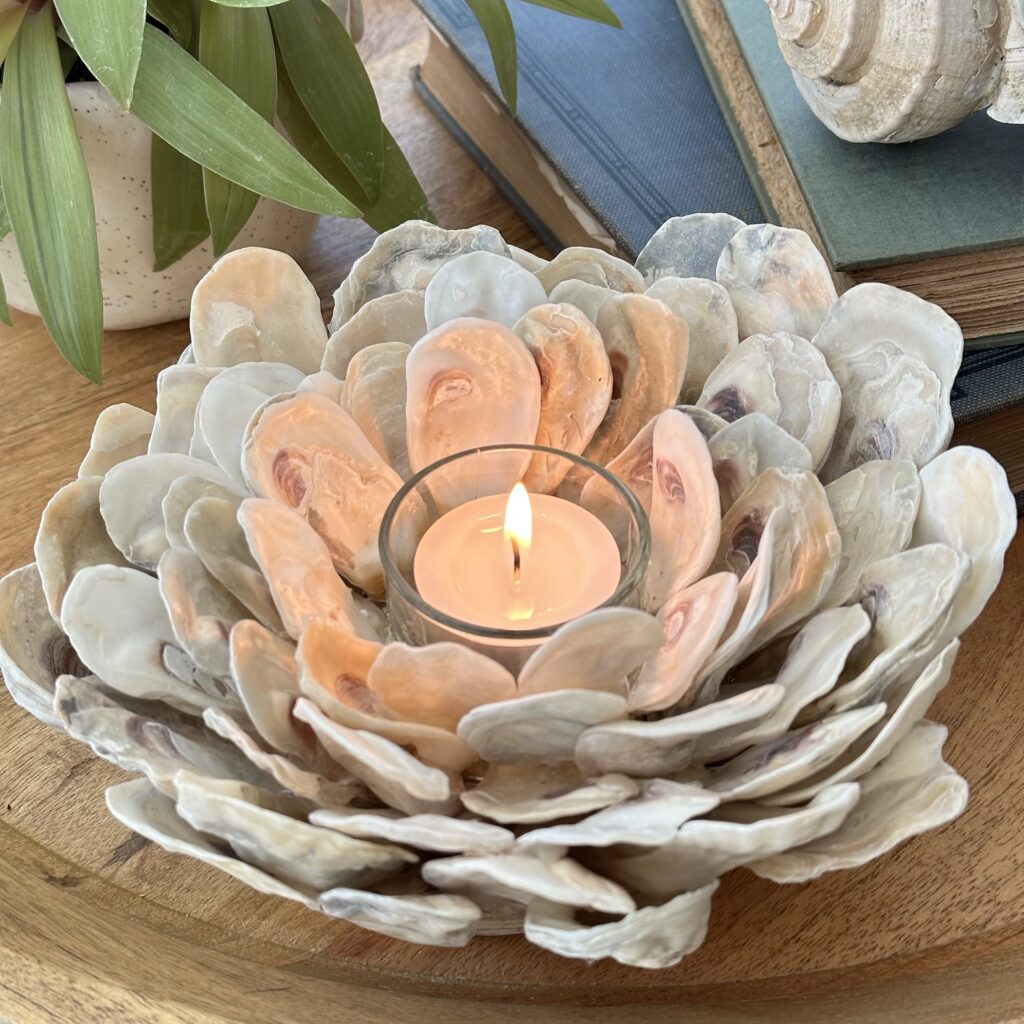 A close up of an oyster shell candle holder with the tea light lit.