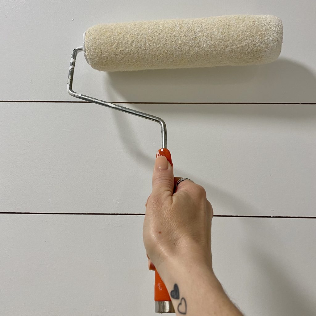 Painting DIY plank wall with white paint on a roller brush.