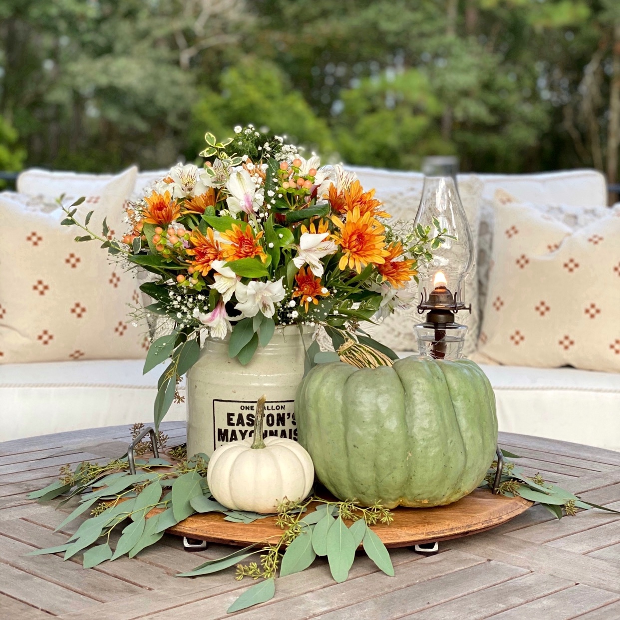 Fall centerpiece on the back patio with a crock filled with Fall flowers, pumpkins, and a vintage glass lantern glowing.