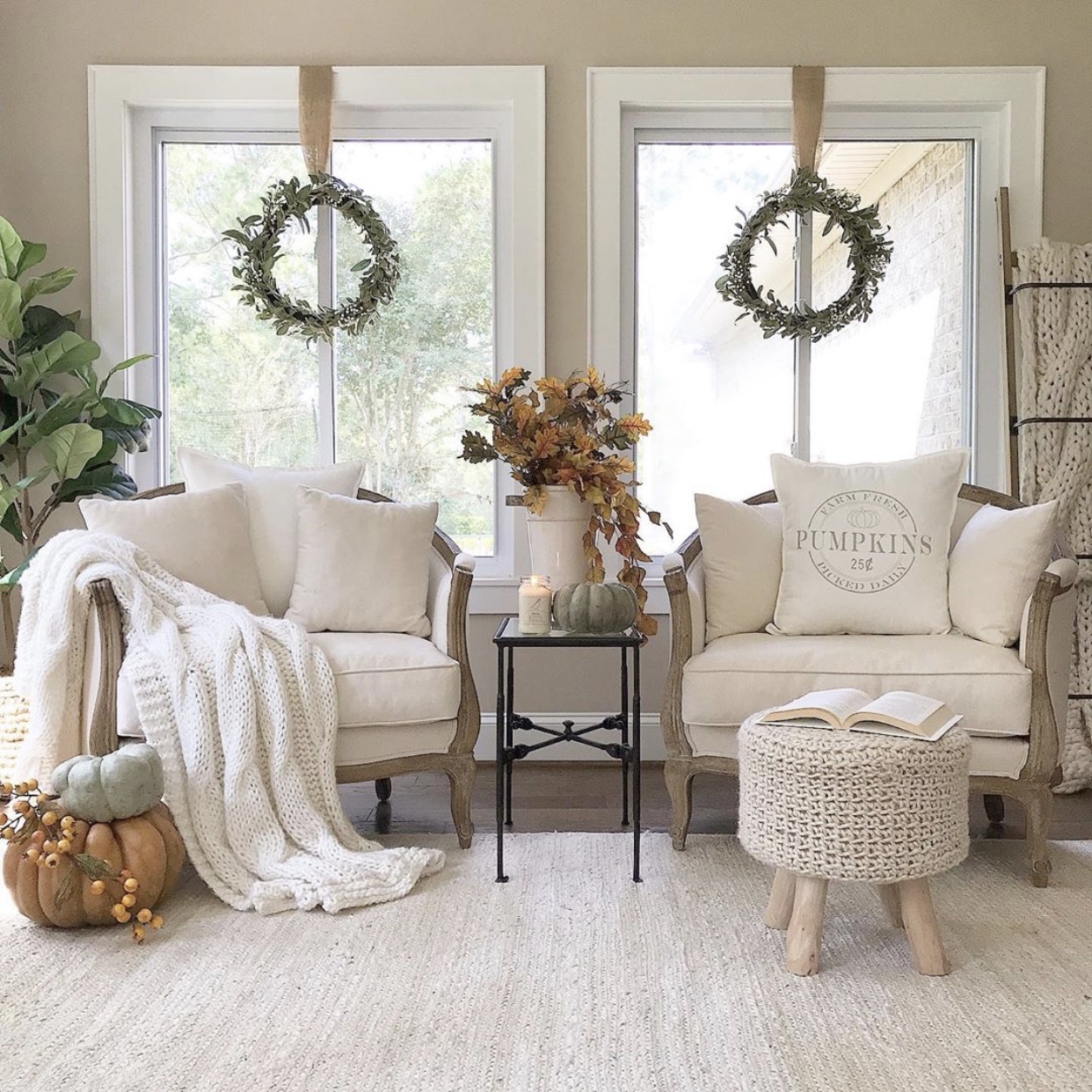 Two chairs in front of two windows with fall decor and a chunky knit neutral throw blanket draped over the arm of a chair.
