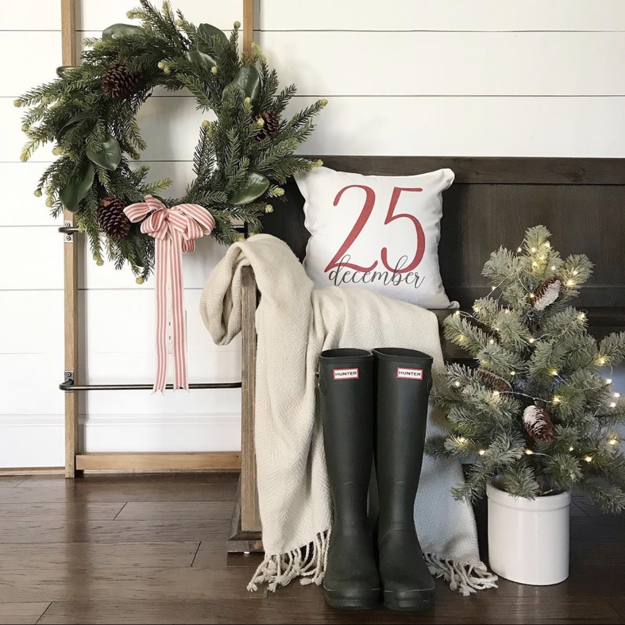 Farmhouse Christmas decor vignette with a wreath, a small Christmas tree, a pillow and blanket.