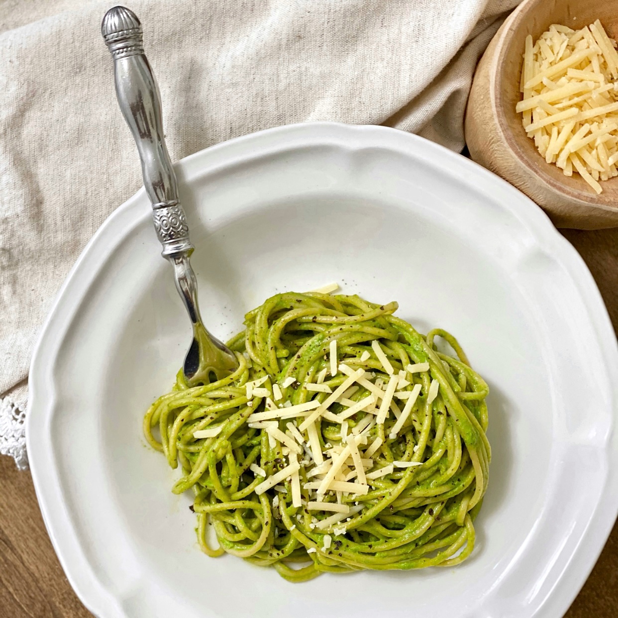 Delicious kale pesto on whole wheat spaghetti pasta with parmesan cheese and fresh cracked pepper on top served in a white pasta bowl.