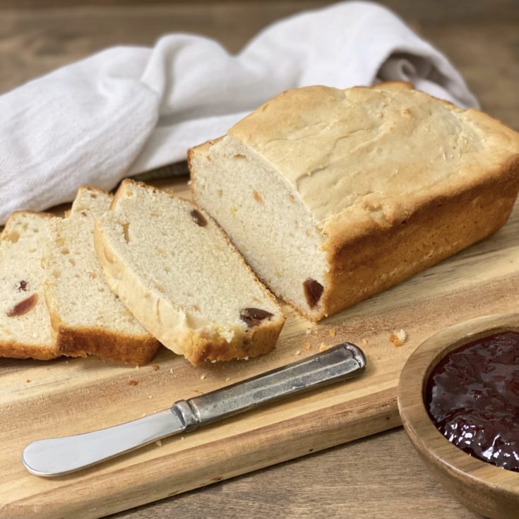 Ice Cream Bread on a bread board sliced with a wood bowl of strawberry jam and a knife next to it.
