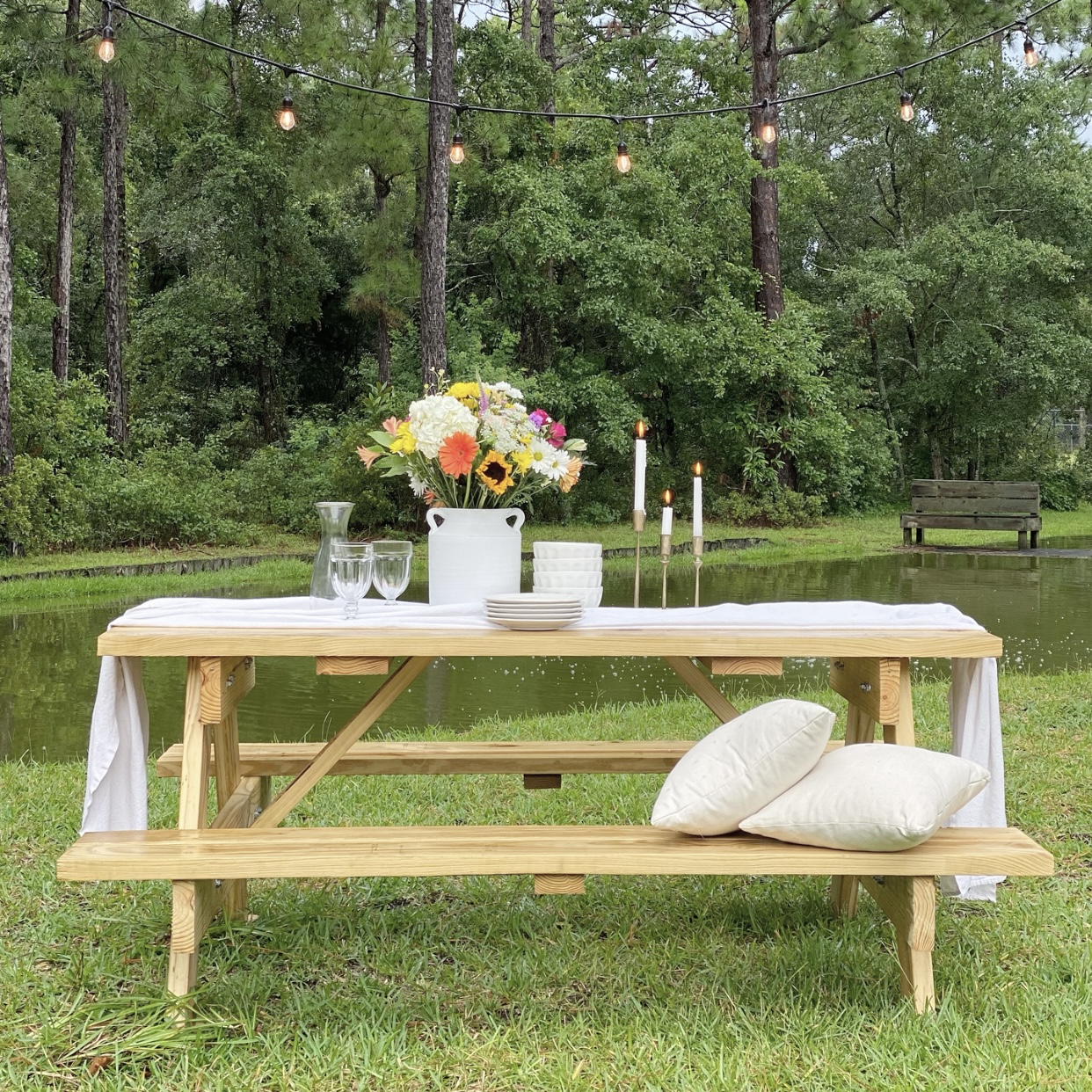 Picnic table next to the pond with a white crock of flowers and white dishes.