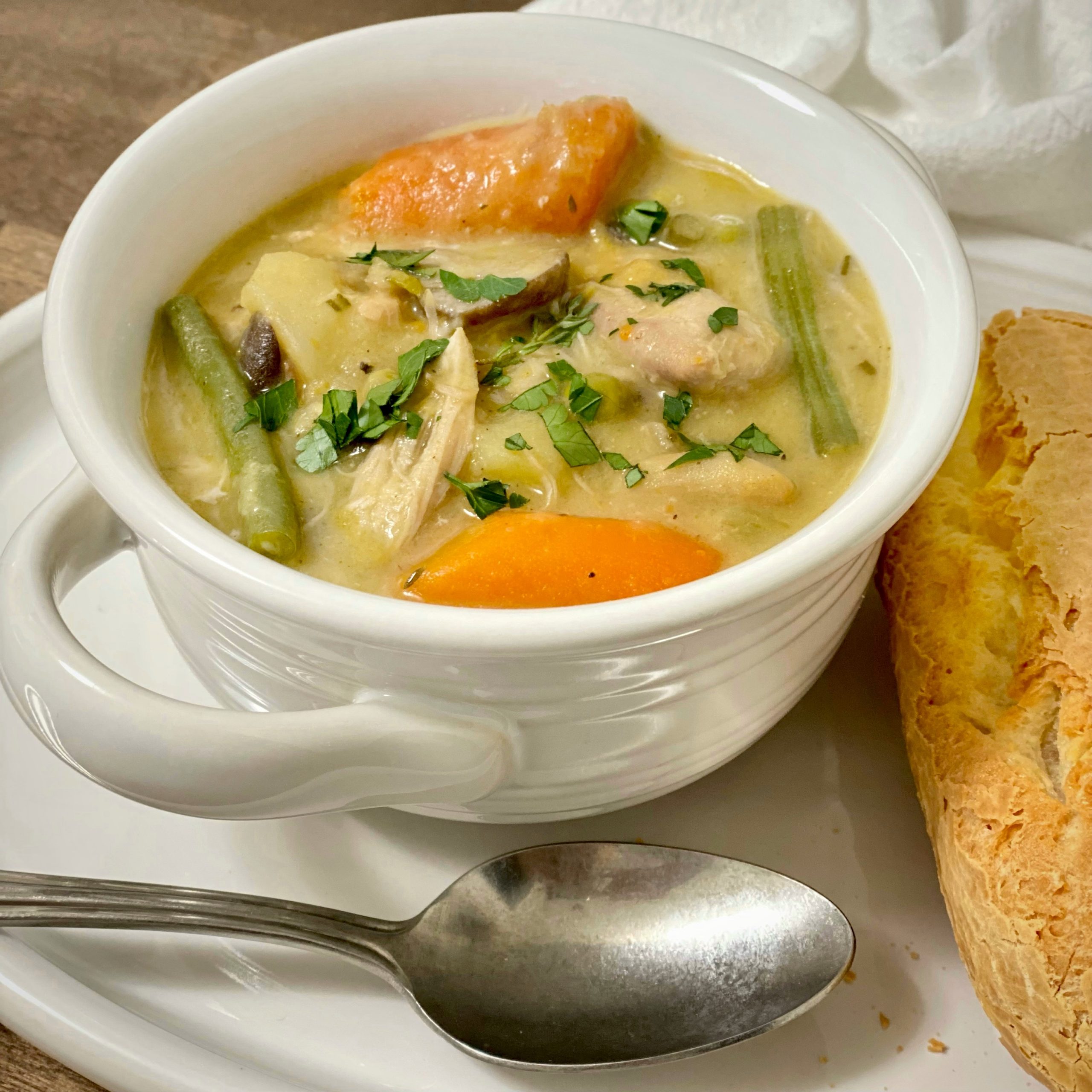 Savory chicken stew in a bowl with a spoon and baguette next to it.