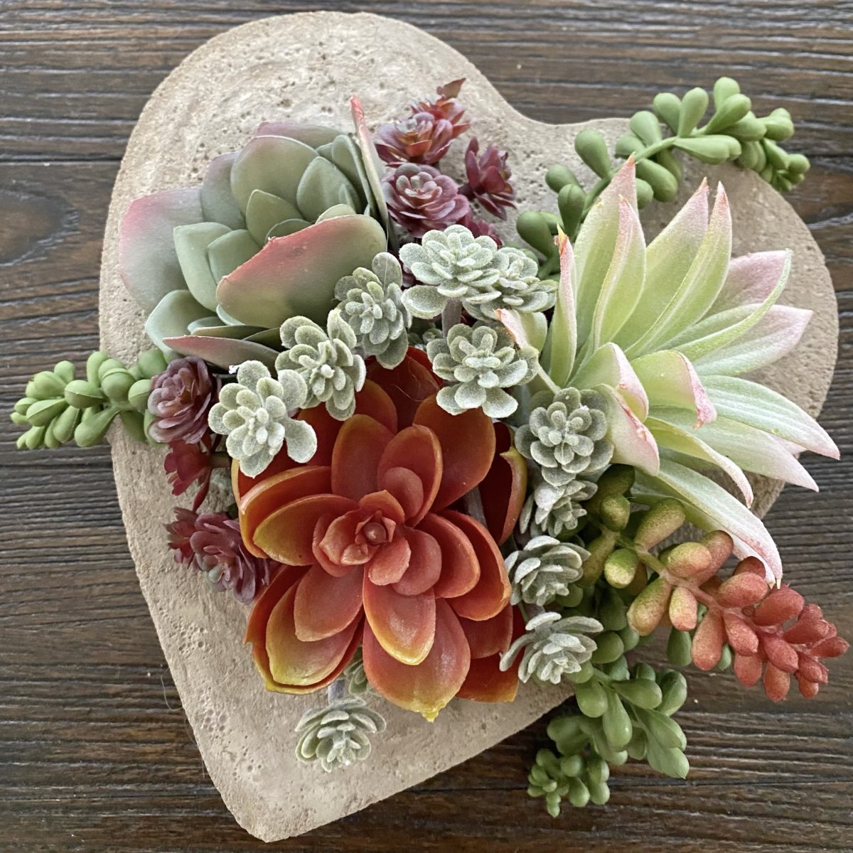 DIY concrete heart planter with a variety of faux succulents arranged in it.