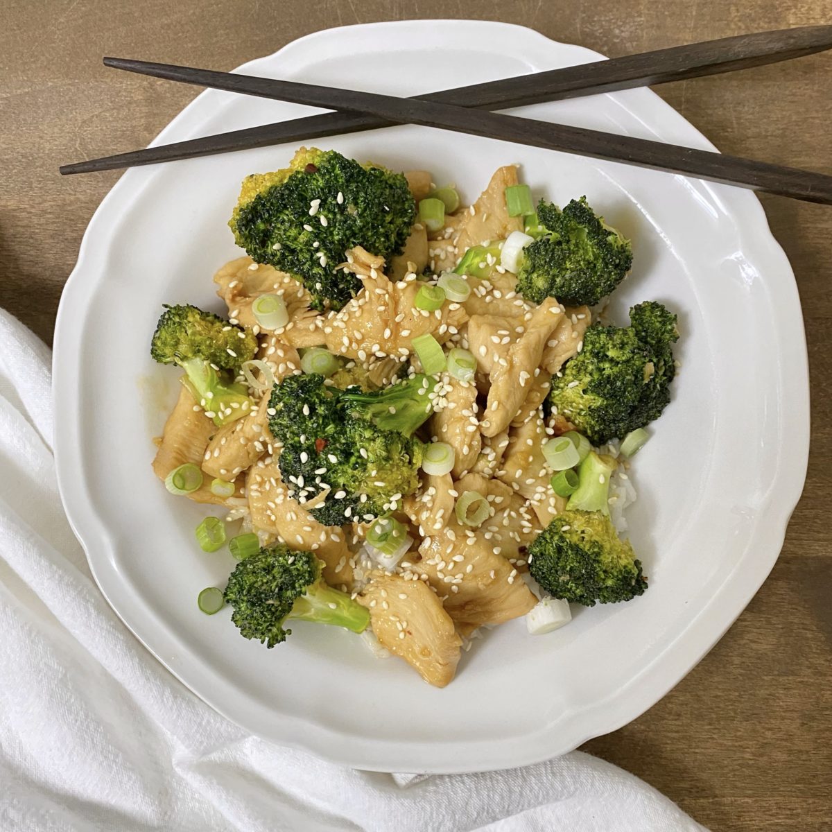 Honey garlic chicken with broccoli in a white bowl with chopsticks on the side.
